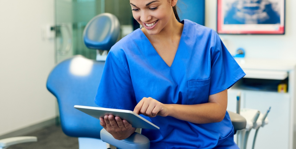 dental nurse in scrubs looking on iPad